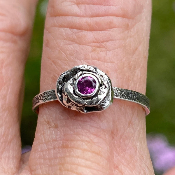 A 3mm, faceted Ruby is ensconced in a thick, organic Sterling Silver bezel setting.  The size 8 band is textured Sterling Silver.  While there are similar rings in this style each is one of a kind due to the organic nature used to create the unique style.  Wear it as a single piece or as part of a stack.  Associated with the Heart Chakra, Ruby is said to stimulate nurturing and spiritual wisdom.   Size 8