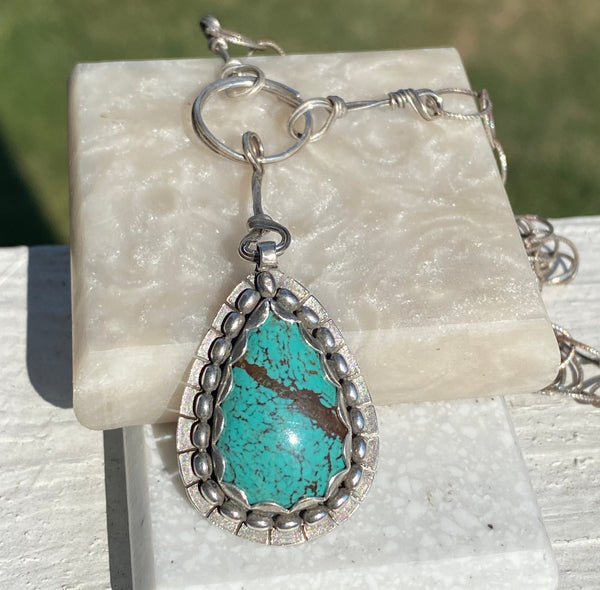 Light blue with brown markings this pear shaped Hubei Turquoise measures 20 x 13mm.  It is set in Sterling Silver and surrounded with oval beads.  Charm:  1.25L x .75(ish)W  Chain:  18" patterned, oxidized 6.4mm cable chain with Lobster clasp.  The addition of handmade embellishments make the chain 22" in length.