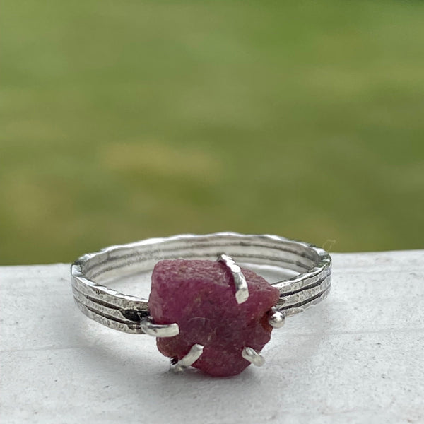 Five Sterling Silver prongs hold a raw Ruby on a textured Sterling Silver band.    Worn by itself or as part of a stack, this July birthstone stands out with its unique shape.  The flat topped Ruby with irregular edges measures 8.80mm x 7.70mm across at it widest points.  It is 3.50mm deep.  Ruby is said to stimulate the Heart Chakra offering nurturing and spiritual wisdom.  Size 7.75