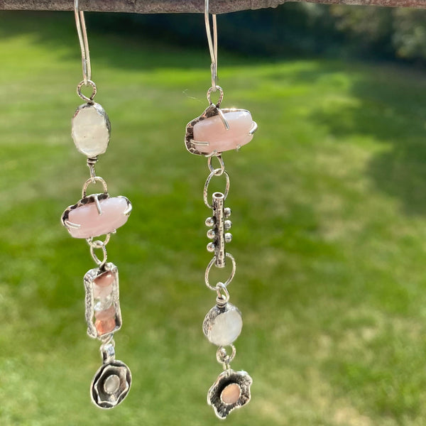 So pretty...eyecatching drama in soft shades of pink and white with rainbow flashes. And like us, these earrings offer so much more than beauty.  They speak to an inner knowing of self and an energy that brings the stars to the soul.
Created with Semiprecious Gemstones and hand crafted Sterling Silver charms.
Two 13.85 x 2.59mm rectangular Pink Opals (prong set)
10mm round Rainbow Moonstone (bezel set)
6mm round Pink Chalcedony (bezel set)
12.5 x 8.7mm oval Rainbow Moonstone (bezel set)
4mm Cat's