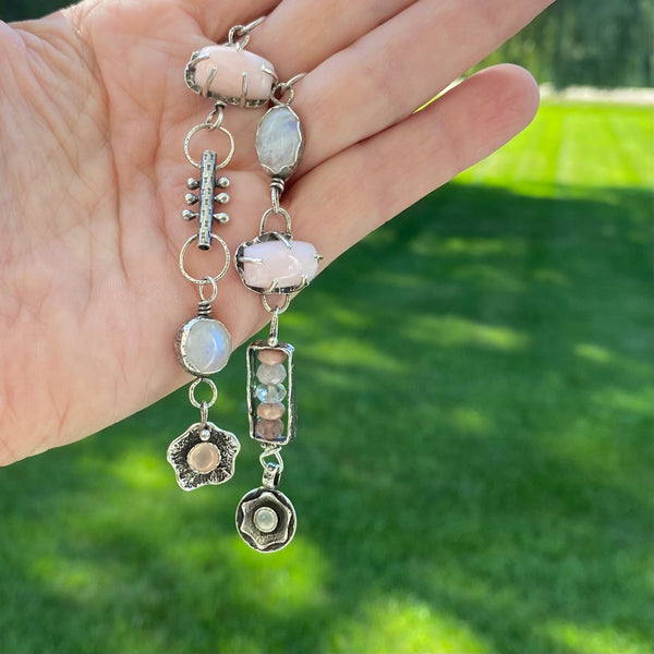 So pretty...eyecatching drama in soft shades of pink and white with rainbow flashes. And like us, these earrings offer so much more than beauty.  They speak to an inner knowing of self and an energy that brings the stars to the soul.
Created with Semiprecious Gemstones and hand crafted Sterling Silver charms.
Two 13.85 x 2.59mm rectangular Pink Opals (prong set)
10mm round Rainbow Moonstone (bezel set)
6mm round Pink Chalcedony (bezel set)
12.5 x 8.7mm oval Rainbow Moonstone (bezel set)
4mm Cat's
