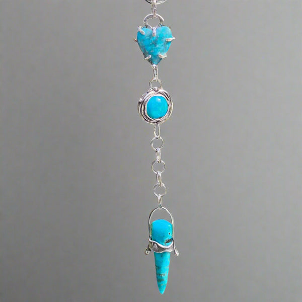 A timeless stone with its variety of colors, Turquoise is said to mean wholeness. Perhaps that is why its popularity continues to rise as we strive to find our footing in this ever changing world!
This trio of blue Turquoise contains touches of black and green. The heart shaped stone, 12mm round stone and elongated triangular stone are set in a variety of textured, patinated Sterling Silver and Argentium™ bezels. 
Charm: 6" long x 3/4" wide
Chain: 21" long textured Sterling