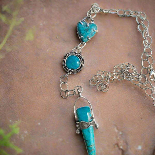 A timeless stone with its variety of colors, Turquoise is said to mean wholeness. Perhaps that is why its popularity continues to rise as we strive to find our footing in this ever changing world!
This trio of blue Turquoise contains touches of black and green. The heart shaped stone, 12mm round stone and elongated triangular stone are set in a variety of textured, patinated Sterling Silver and Argentium™ bezels. 
Charm: 6" long x 3/4" wide
Chain: 21" long textured Sterling