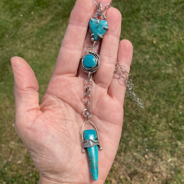 A timeless stone with its variety of colors, Turquoise is said to mean wholeness. Perhaps that is why its popularity continues to rise as we strive to find our footing in this ever changing world!
This trio of blue Turquoise contains touches of black and green. The heart shaped stone, 12mm round stone and elongated triangular stone are set in a variety of textured, patinated Sterling Silver and Argentium™ bezels.
Charm: 6" long x 3/4" wide
Chain: 21" long textured Sterling