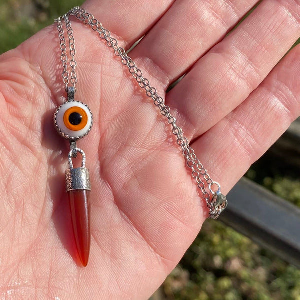 "Since one is love, there is nothing to do but offer love-each offer of love bringing an exponential increase in the quantity of love returned" Melody (Love is in the Earth).
An orange Carnelian point dangles from an orange, 10mm glass "eye".  Both are set in textured and oxidized bezels.
Wearing this talisman can open your eyes to your ability to give and receive love of all varieties.
Charm: 2" long x 1/2" wide
Chain: 16" Sterling Silver 2mm patterned and oxidized cable chain with lobster clasp