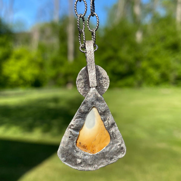 The focal point of this three stone charm is a beautifully patterned Sonoran Dendritic Jasper.  Mostly golden yellow with bits of black, deep orange and sky blue, it brings to mind a volcanic fire rising to the sky.  A round, black beach stone and faceted Sky Blue Topaz complete the trio.
Held in place with prongs, the Sonoran Dendritic is an irregularly shaped triangular stone with a curved bottom and measures 1" in length and .75" in width.  An 8mm Lake Michigan beach stone tops the piece