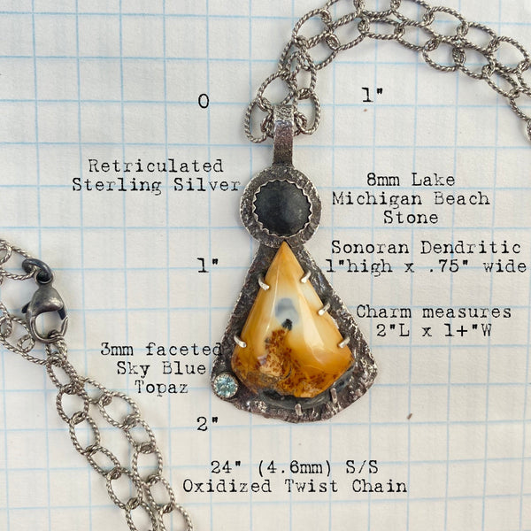 The focal point of this three stone charm is a beautifully patterned Sonoran Dendritic Jasper.  Mostly golden yellow with bits of black, deep orange and sky blue, it brings to mind a volcanic fire rising to the sky.  A round, black beach stone and faceted Sky Blue Topaz complete the trio.
Held in place with prongs, the Sonoran Dendritic is an irregularly shaped triangular stone with a curved bottom and measures 1" in length and .75" in width.  An 8mm Lake Michigan beach stone tops the piece