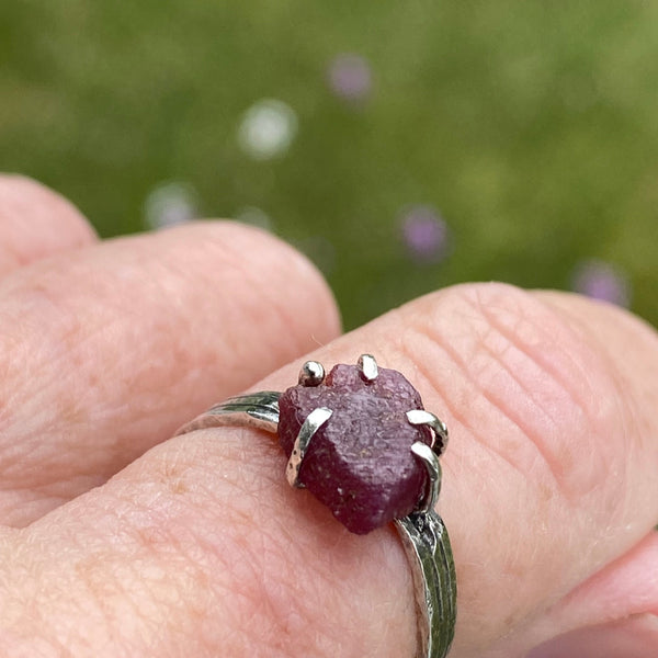 Five Sterling Silver prongs hold a raw Ruby on a textured Sterling Silver band.    Worn by itself or as part of a stack, this July birthstone stands out with its unique shape.  The flat topped Ruby with irregular edges measures 8.80mm x 7.70mm across at it widest points.  It is 3.50mm deep.  Ruby is said to stimulate the Heart Chakra offering nurturing and spiritual wisdom.  Size 7.75