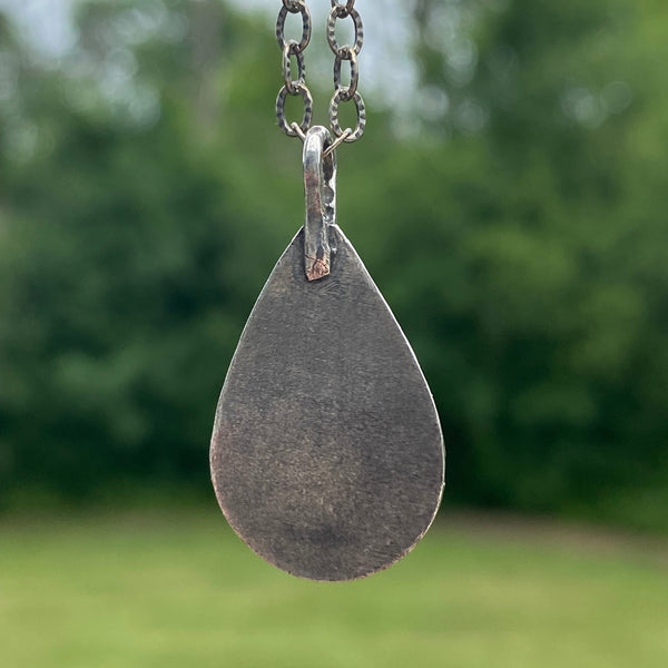 Offering wholeness, the 17 x 10mm pear-shaped Hubei Turquoise has a beautiful color palette of orange, green and blue organic shaped spots on a black background.  It is set in texturized and patinated Sterling Silver.  Charm:  1.25"L x .75"W  Chain:  17" L, 2.8mm oxidized and patterned cable chain