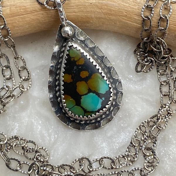 Offering wholeness, the 17 x 10mm pear-shaped Hubei Turquoise has a beautiful color palette of orange, green and blue organic shaped spots on a black background.  It is set in texturized and patinated Sterling Silver.
Charm:  1.25"L x .75"W
Chain:  17" L, 2.8mm oxidized and patterned cable chain