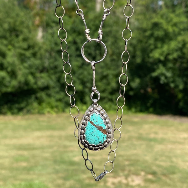 Light blue with brown markings this pear shaped Hubei Turquoise measures 20 x 13mm.  It is set in Sterling Silver and surrounded with oval beads.  Charm:  1.25L x .75(ish)W  Chain:  18" patterned, oxidized 6.4mm cable chain with Lobster clasp.  The addition of handmade embellishments make the chain 22" in length.