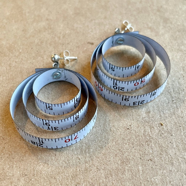 A wonderful flea market find inspired me to make these earrings based on a 1990's Nike ad (see blog).  Somewhat of a limited edition because that's what happens with found objects.  When they're gone, they are gone.  Made from vintage tape measures, micro-screws hold the three concentric loops of each earring together.  Charm:  1.5" length, 1.25" width (approx. 1 1/8" diameter)  Total length:  1.5"  Sterling Silver posts