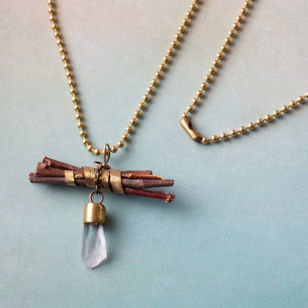 “Wisdom begins in wonder” (Socrates) is stamped on a brass band that wraps around a bundle of sticks on this handmade necklace.  Flashing light as it moves, a Quartz crystal dangles on a small, brass chain.