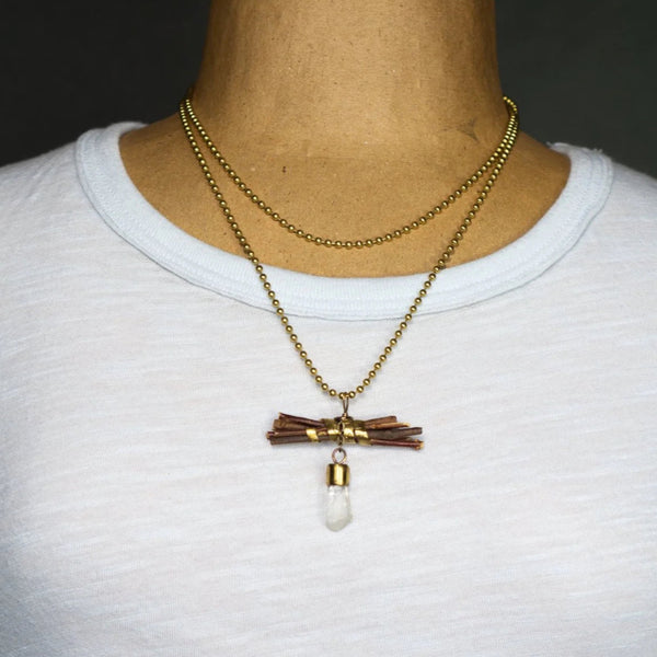 “Wisdom begins in wonder” (Socrates) is stamped on a brass band that wraps around a bundle of sticks on this handmade necklace.  Flashing light as it moves, a Quartz crystal dangles on a small, brass chain.