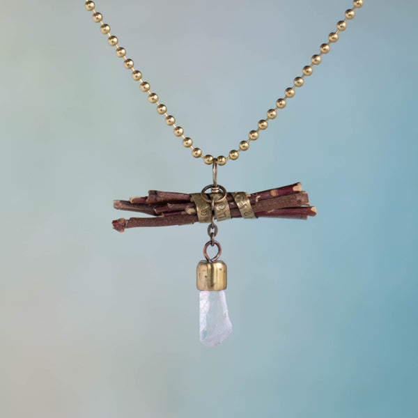 “Wisdom begins in wonder” (Socrates) is stamped on a brass band that wraps around a bundle of sticks on this handmade necklace.  Flashing light as it moves, a Quartz crystal dangles on a small, brass chain.