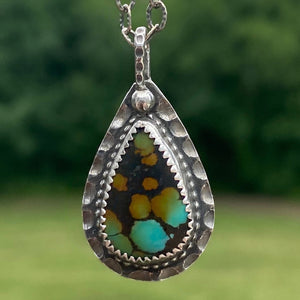 Offering wholeness, the 17 x 10mm pear-shaped Hubei Turquoise has a beautiful color palette of orange, green and blue organic shaped spots on a black background.  It is set in texturized and patinated Sterling Silver.  Charm:  1.25"L x .75"W  Chain:  17" L, 2.8mm oxidized and patterned cable chain