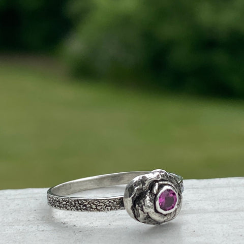 A 3mm, faceted Ruby is ensconced in a thick, organic Sterling Silver bezel setting.  The size 8 band is textured Sterling Silver.  While there are similar rings in this style each is one of a kind due to the organic nature used to create the unique style.  Wear it as a single piece or as part of a stack.  Associated with the Heart Chakra, Ruby is said to stimulate nurturing and spiritual wisdom.   Size 8