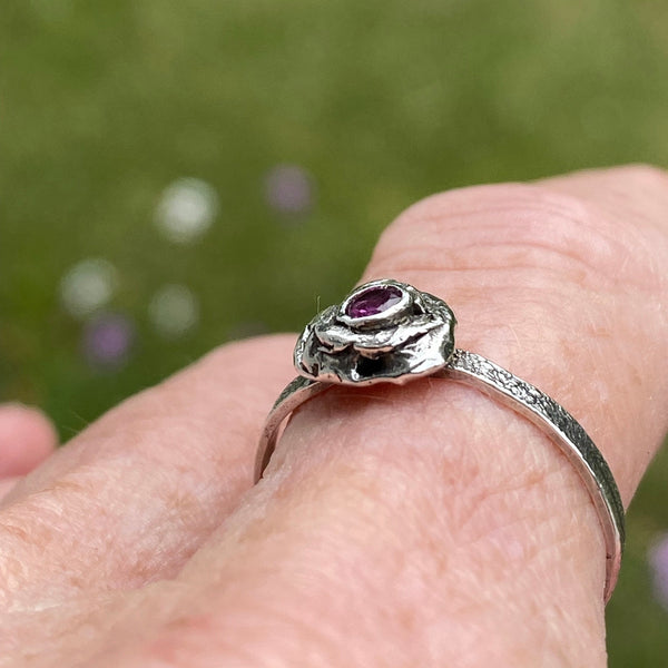 A 3mm, faceted Ruby is ensconced in a thick, organic Sterling Silver bezel setting.  The size 8 band is textured Sterling Silver.  While there are similar rings in this style each is one of a kind due to the organic nature used to create the unique style.  Wear it as a single piece or as part of a stack.  Associated with the Heart Chakra, Ruby is said to stimulate nurturing and spiritual wisdom.   Size 8