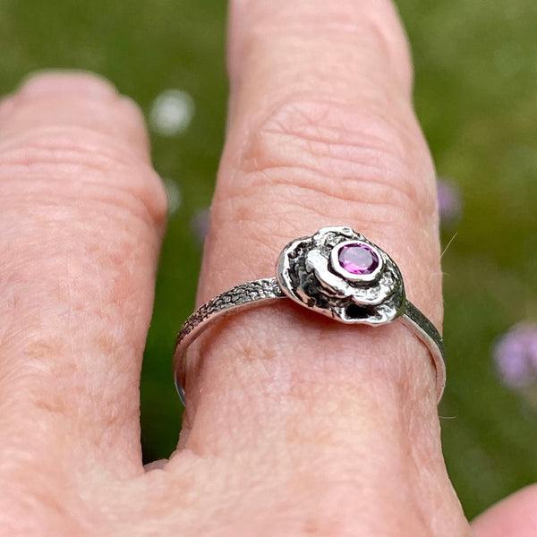 A 3mm, faceted Ruby is ensconced in a thick, organic Sterling Silver bezel setting.  The size 8 band is textured Sterling Silver.  While there are similar rings in this style each is one of a kind due to the organic nature used to create the unique style.  Wear it as a single piece or as part of a stack.  Associated with the Heart Chakra, Ruby is said to stimulate nurturing and spiritual wisdom.   Size 8