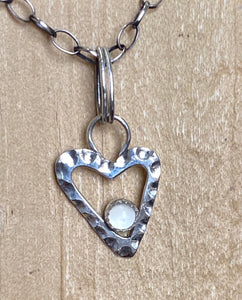A 3mm Cat's Eye Moonstone nests in a textured Sterling Silver heart.  This semi-precious gemstone is said to offer serenity and happiness.  Charm:  5/8" x 1/4" Sterling Silver heart with a 3mm Cat's Eye Moonstone  Chain:  19" Sterling Silver 2.5mm oval rollo chain